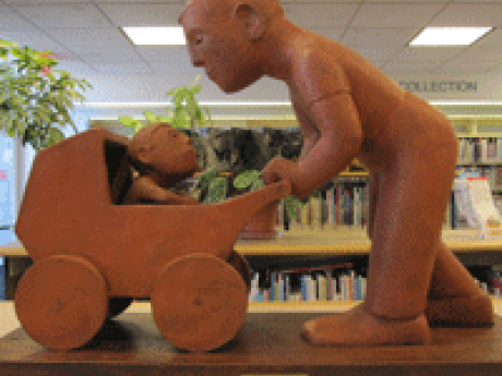 Terra cotta sculpture depicting father pushing son in a stroller